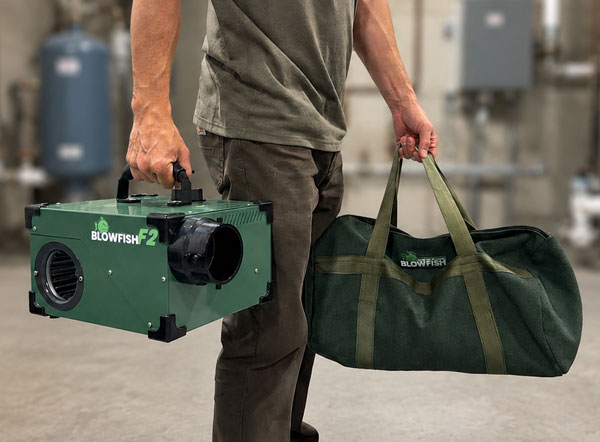 Professional plumber carrying a Blowfish F2 plumbing smoke blower and hose & accessory bag